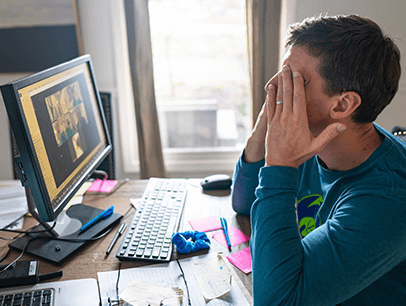 Man in front of computer with hands over eyes