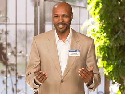 Man in tan suit jacket speaking with gestures